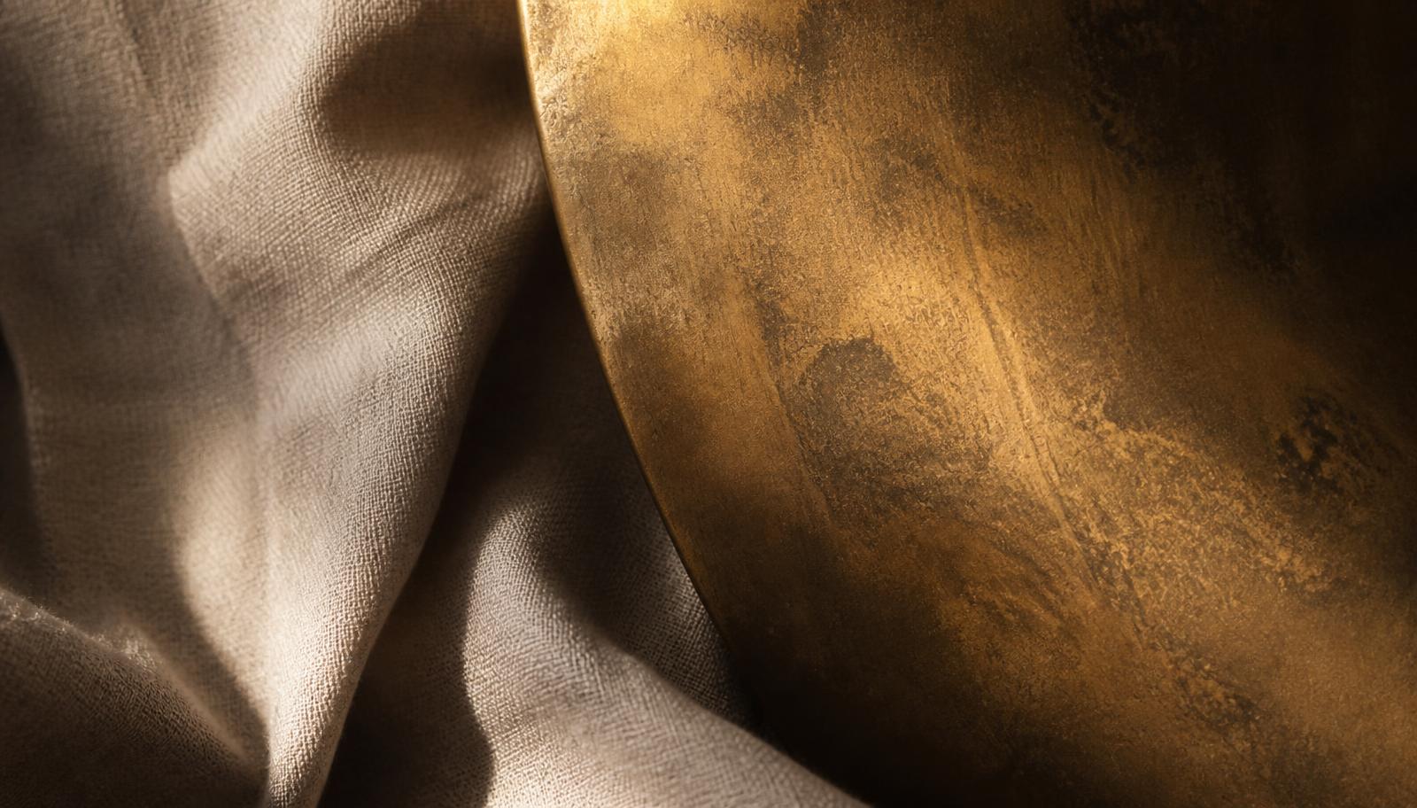 Close-up of linen napkin folds beside an aged brass tray lit with warm amber light